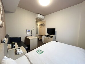 A hotel room with a bed, a desk with a computer, a TV, and a small seating area.