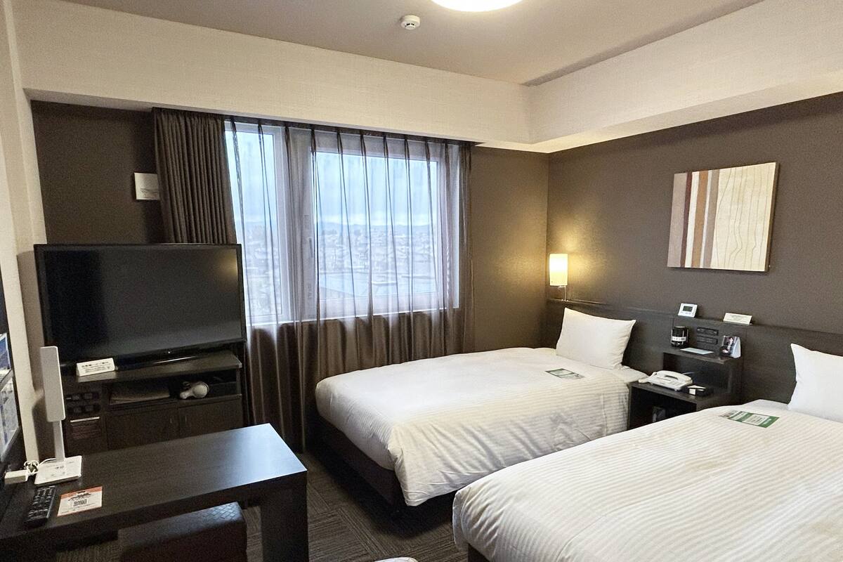 Ein Hotelzimmer mit zwei Betten, einem Schreibtisch mit Fernseher, einem kleinen Tisch und einem Nachttisch mit Telefon und Lampe.