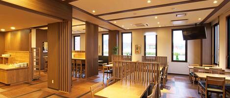 A spacious restaurant with wooden furniture, large windows, and a flat-screen TV.
