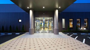 A modern building entrance with a tiled floor, large pillars, and glass doors leading inside.