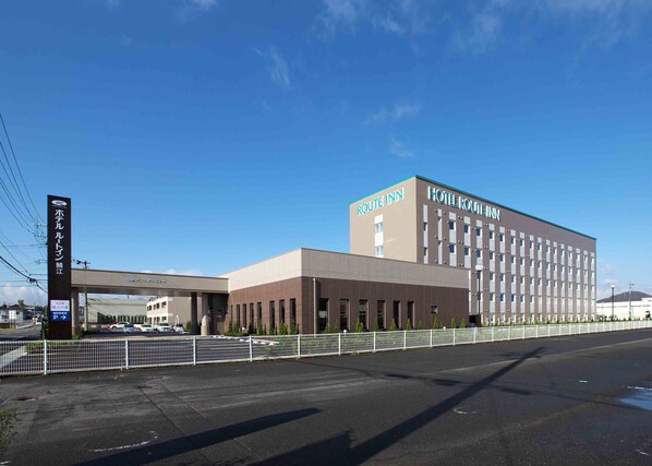 A Route Inn hotel with a modern design, featuring a large parking lot and a clear sky.