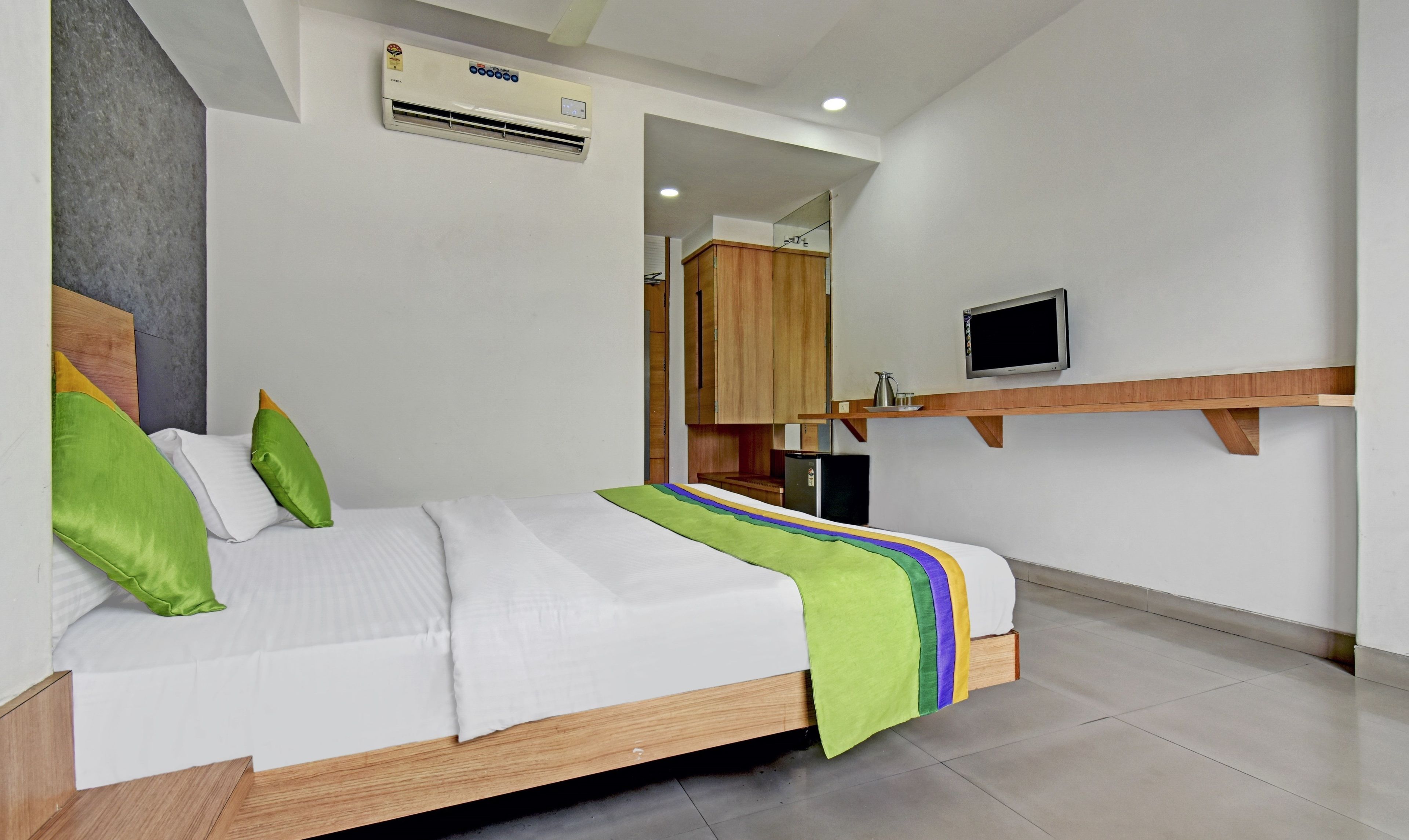 A modern hotel room with a bed, a television, and a kitchenette.