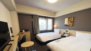Une chambre d’hôtel avec deux lits, un bureau avec une chaise, une petite table, un téléviseur et une fenêtre avec des rideaux.