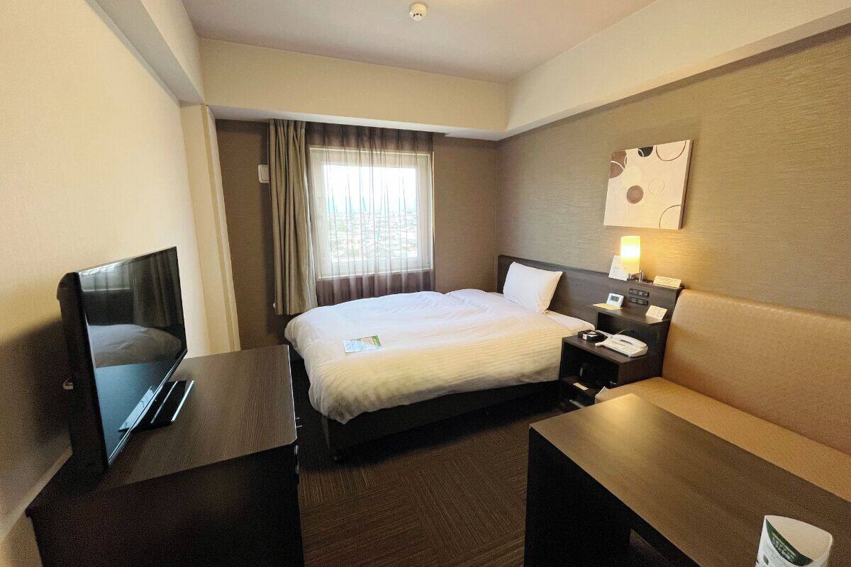 A hotel room with a bed, bedside table, TV, and a desk.