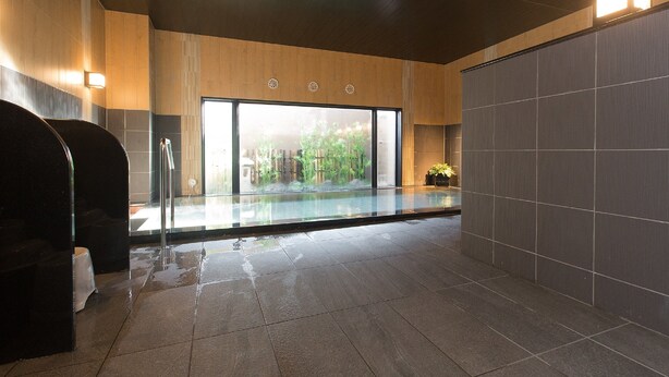 Une salle de bain moderne avec une douche à l’italienne en verre, une grande fenêtre donnant sur un espace verdoyant et un sol carrelé.