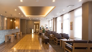Un hall d’hôtel moderne avec un revêtement de sol en bois, des espaces aménagés pour s’asseoir et un comptoir d’accueil.