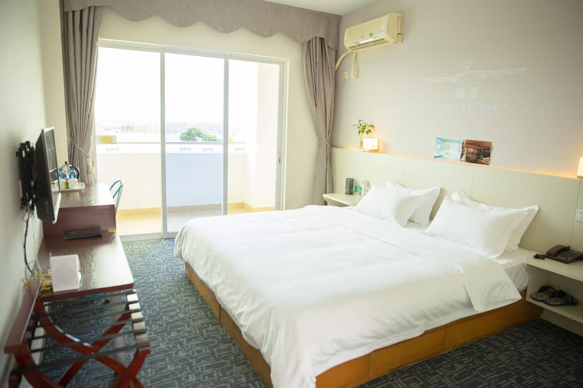 A hotel room with a bed, a desk with a computer, a chair, a TV, and a window with curtains.