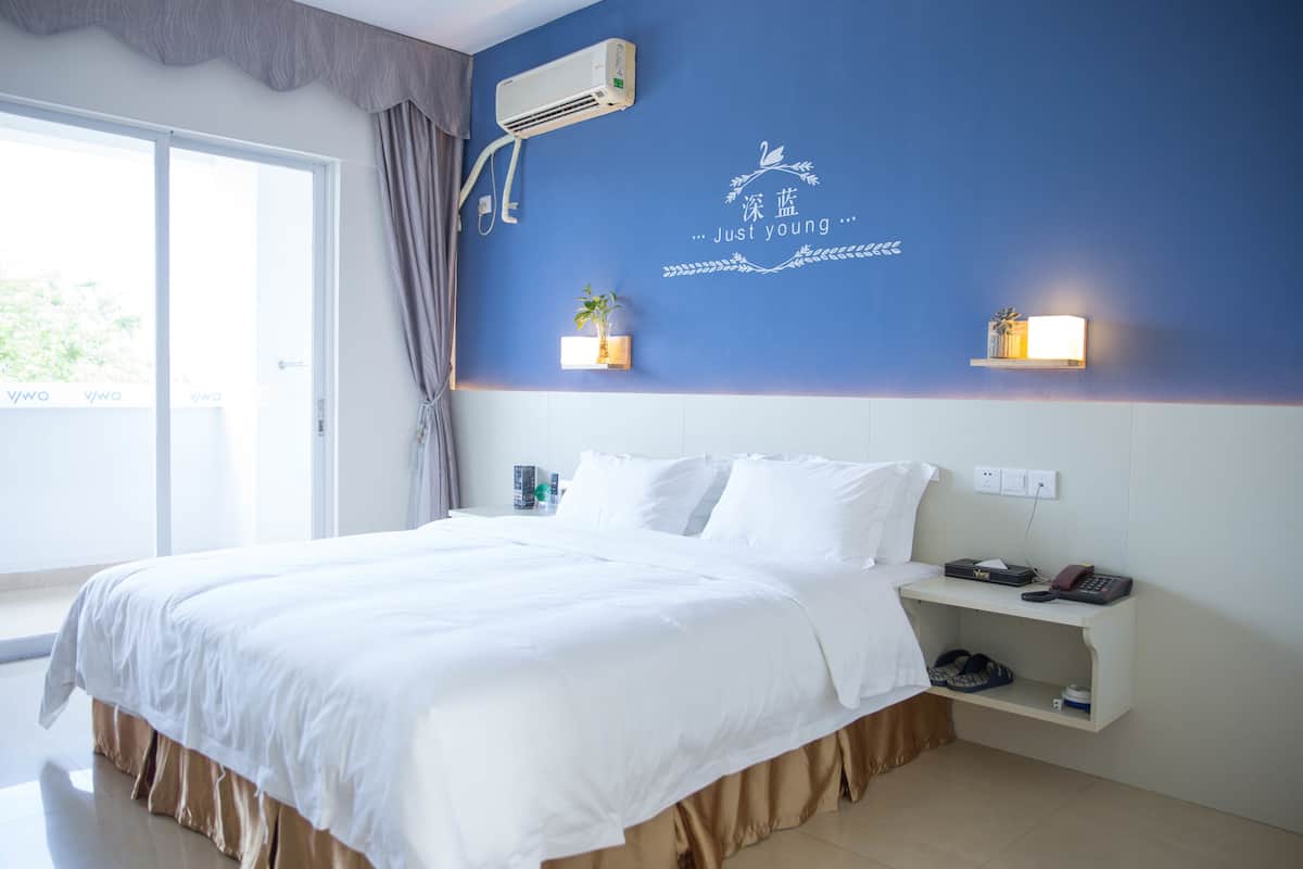 A hotel room with a large bed, a bedside table with a lamp, and a wall-mounted air conditioner.
