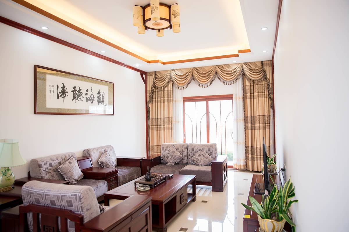 A living room with a sofa set, a coffee table, and a television. There is a framed artwork on the wall and a window with curtains.