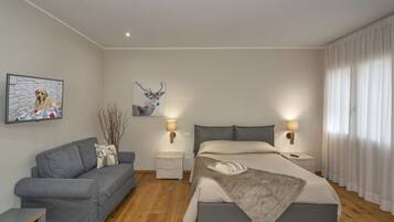 Quarto moderno com um sofá cinzento, uma cama grande com manta cinza, duas mesas de cabeceira com abajures, e uma parede com duas fotografias emolduradas.
