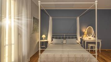 A four-poster bed with a canopy, bedside tables with lamps, a mirror, and a small stool.