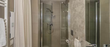 A modern bathroom with a glass-enclosed shower, a large mirror, and a wooden vanity with toiletries.