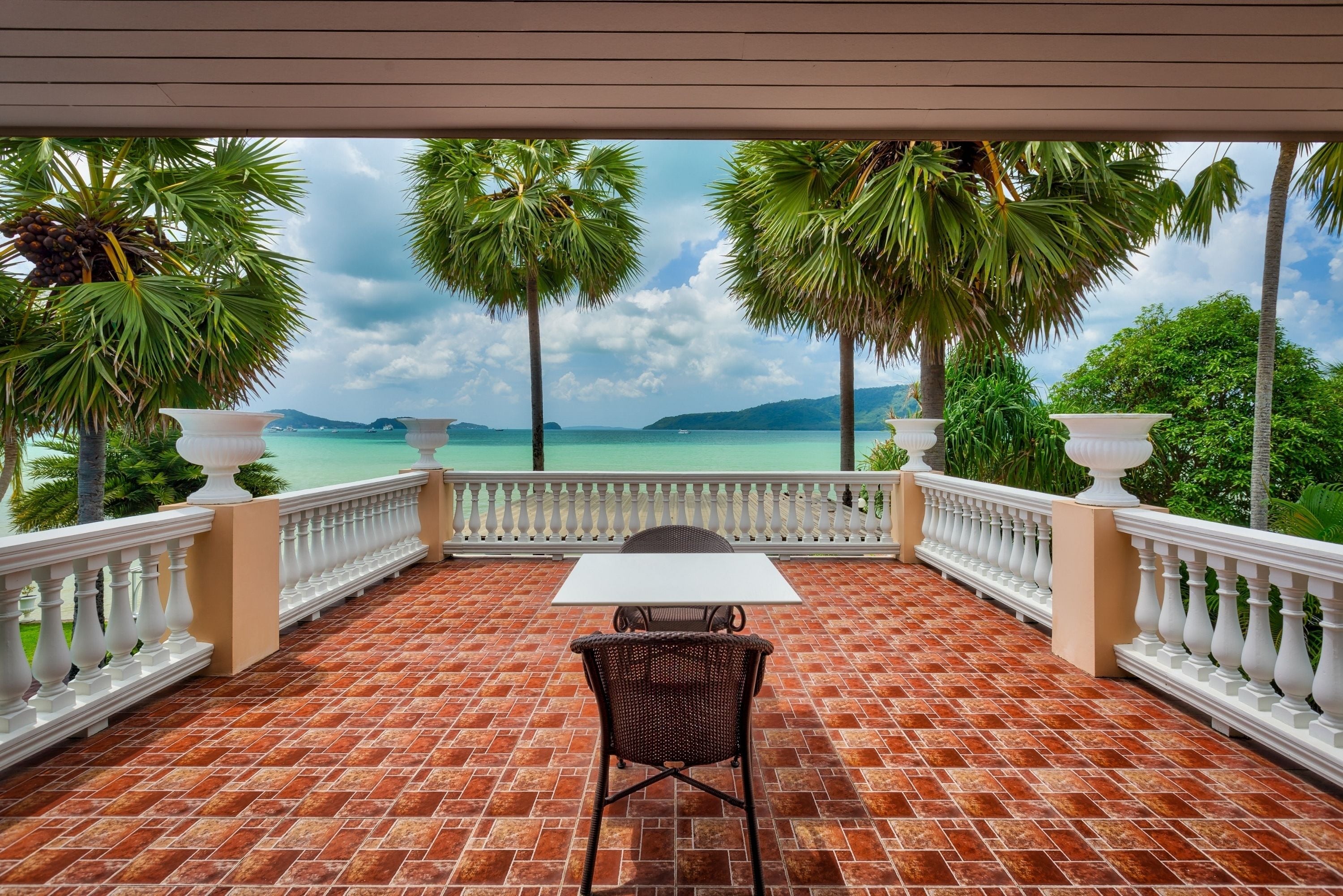 Una terraza con una mesa y sillas, con vista al mar turquesa y palmeras.