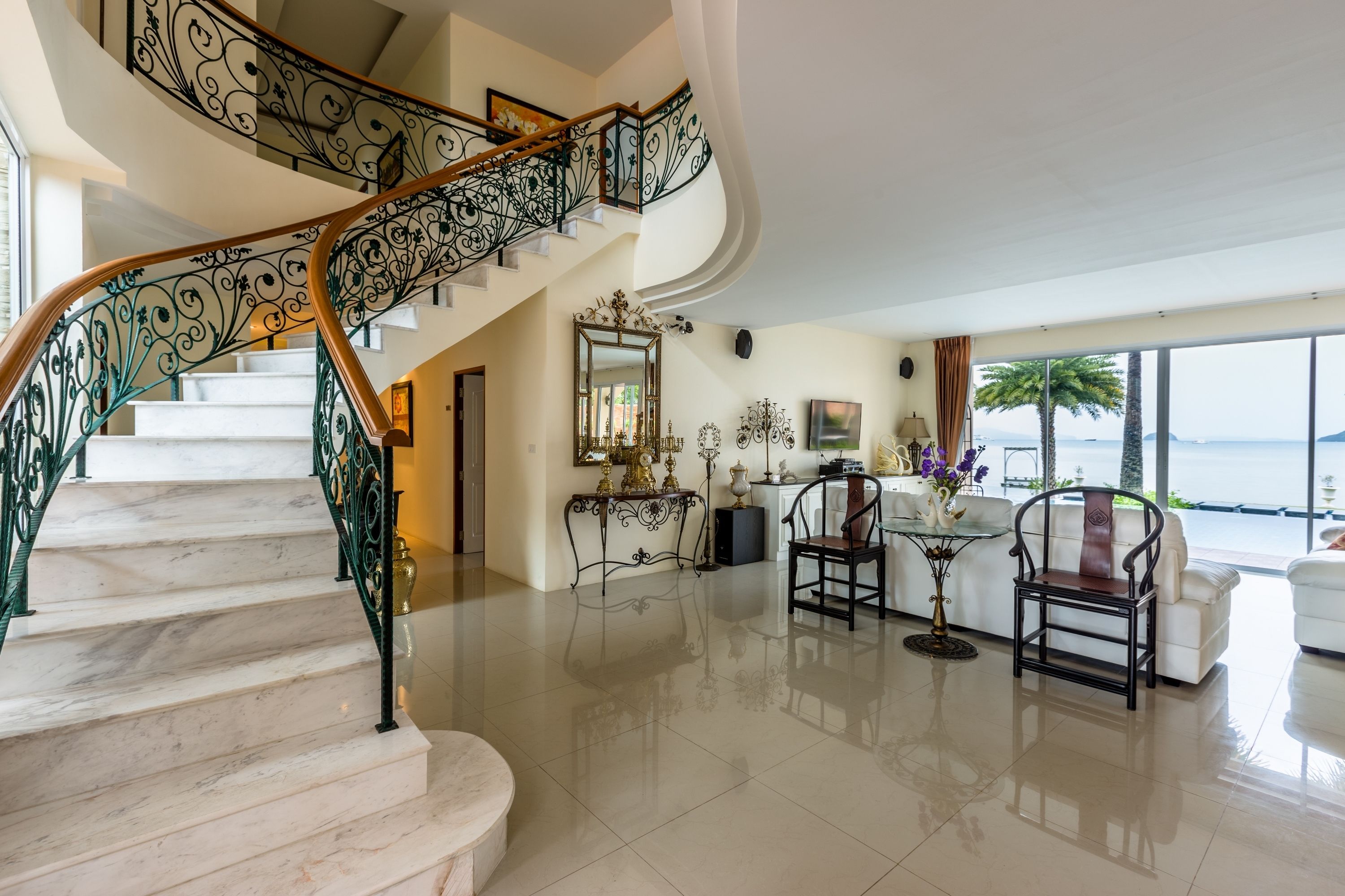 A spacious living area with a marble staircase, a large window offering a view of the sea, and a seating area with a coffee table and chairs.