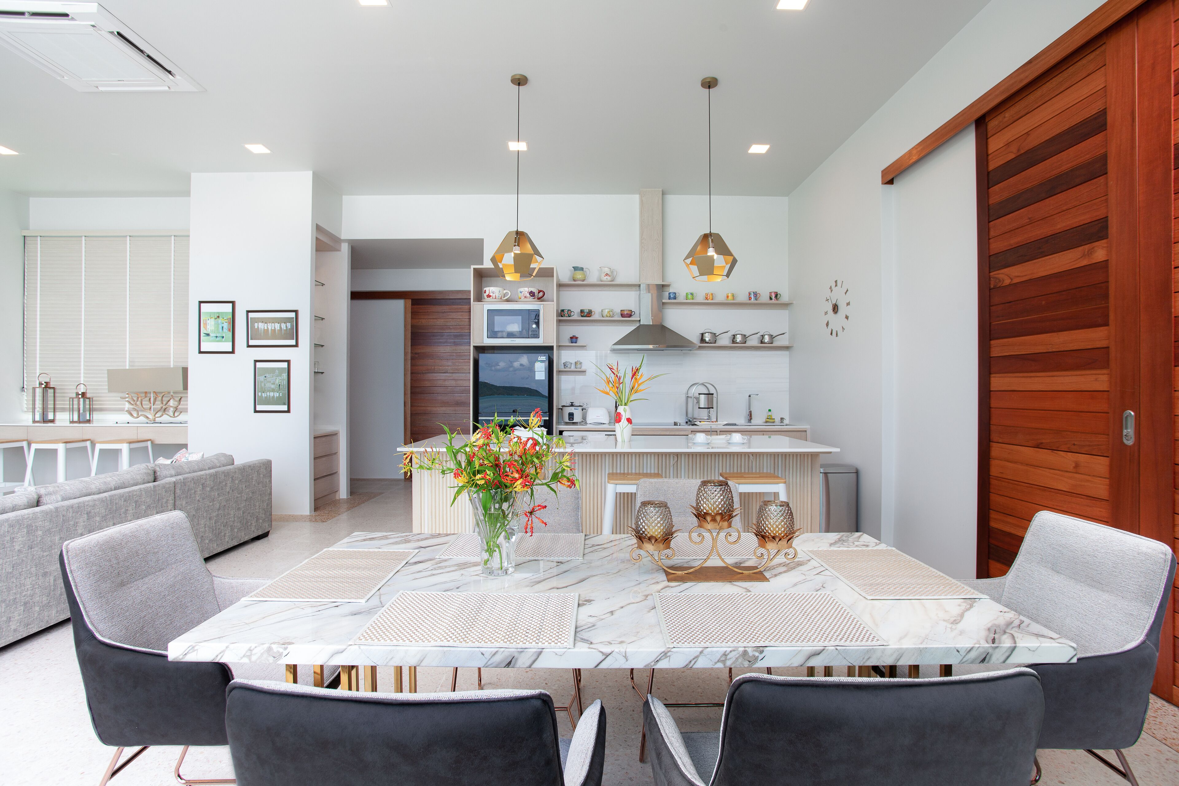 A modern kitchen with a central island, white cabinetry, and a dining area with a marble table and chairs.