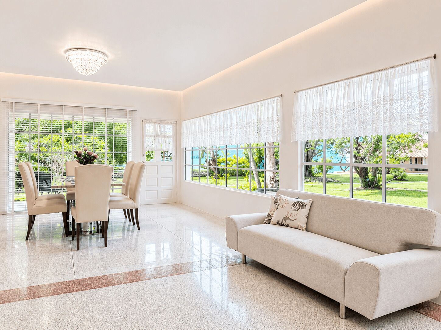 A spacious room with a dining area, a sofa, and large windows with curtains.