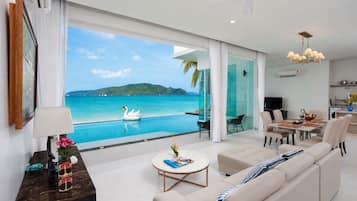 A modern living room with a large window overlooking a pool and ocean view, a dining area, and a kitchen.