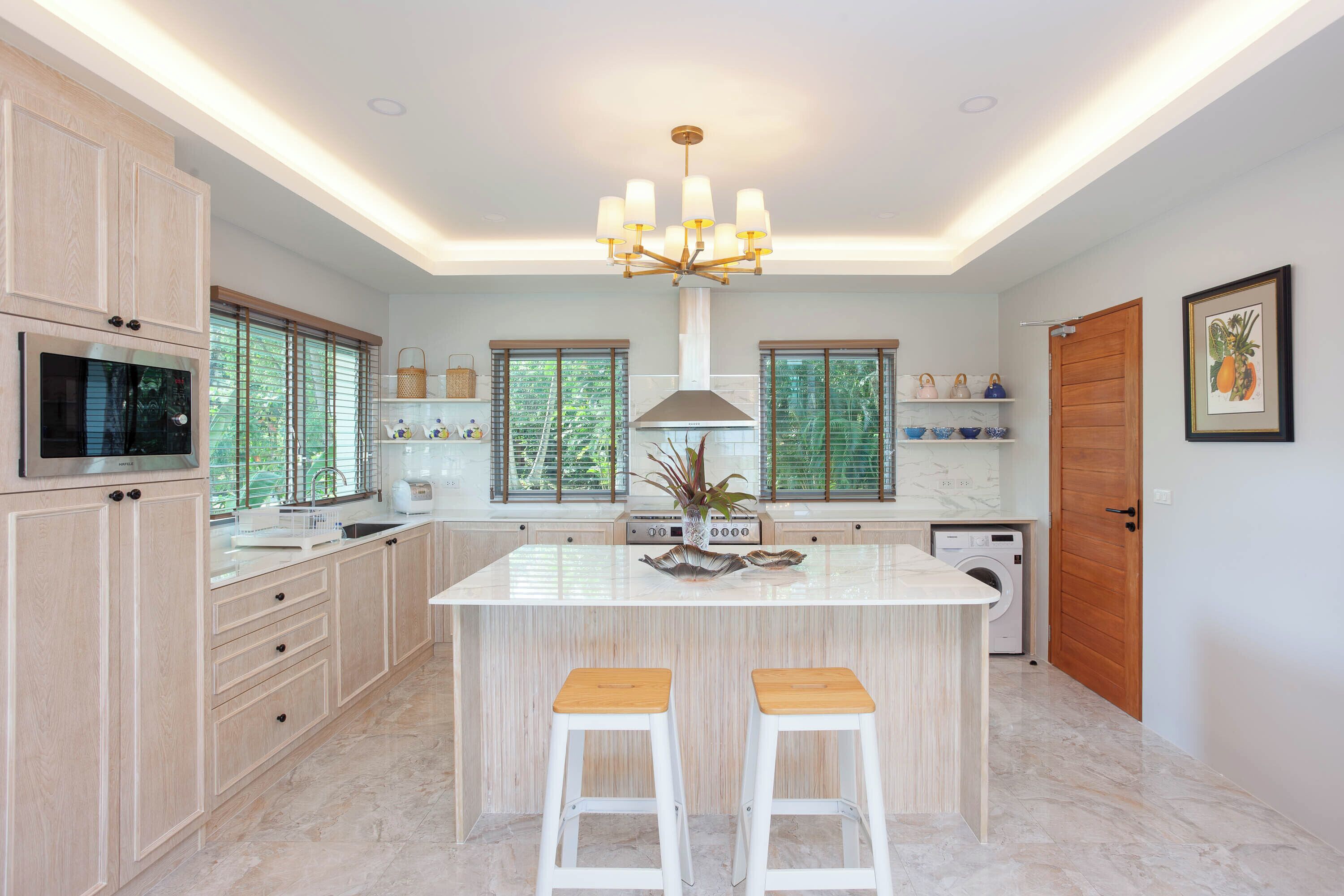 A modern kitchen with a central island, white cabinetry, a built-in microwave, and a chandelier.