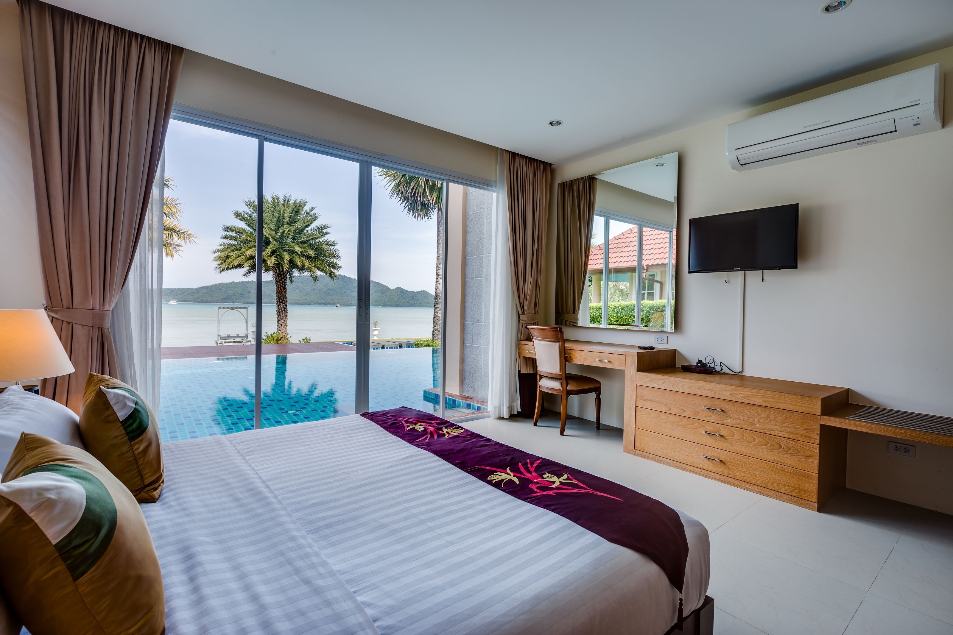A hotel room with a large bed, a desk, a chair, a TV, and a view of a pool and mountains.