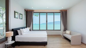 Un dormitorio con cama, sofá, mesita de noche y un ventanal con vista al mar.