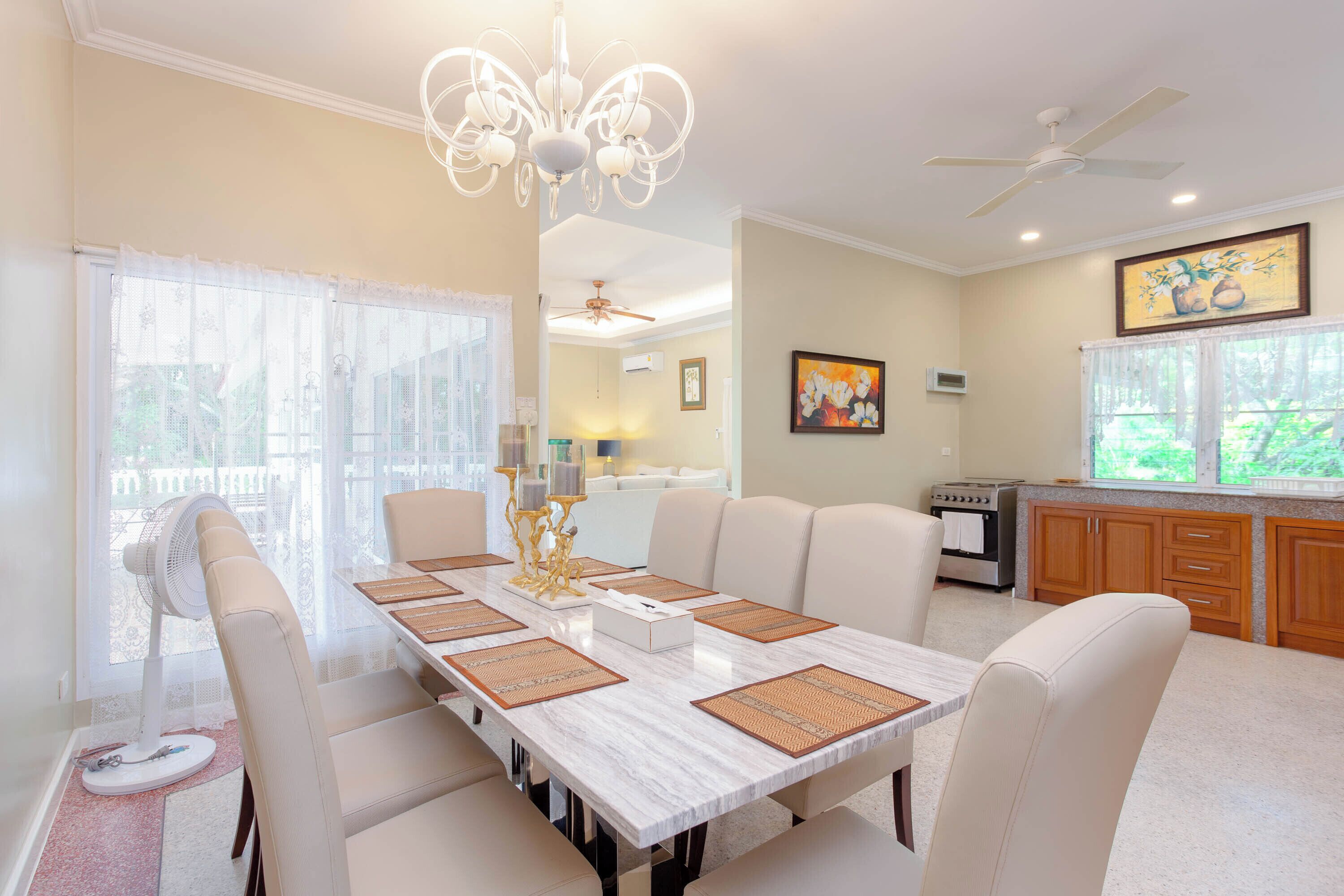 A dining area with a marble table, white chairs, and a ceiling fan.
