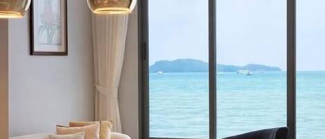 A modern room with a white sofa, a black chair, and a large window overlooking the sea.