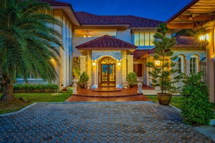 A two-story house with a tiled roof, a stone entrance, and a paved driveway.