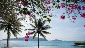 A poolside area with two palm trees and pink flowers, overlooking a calm sea with distant mountains. - Fisherman Way Beach Villa (Rawai)