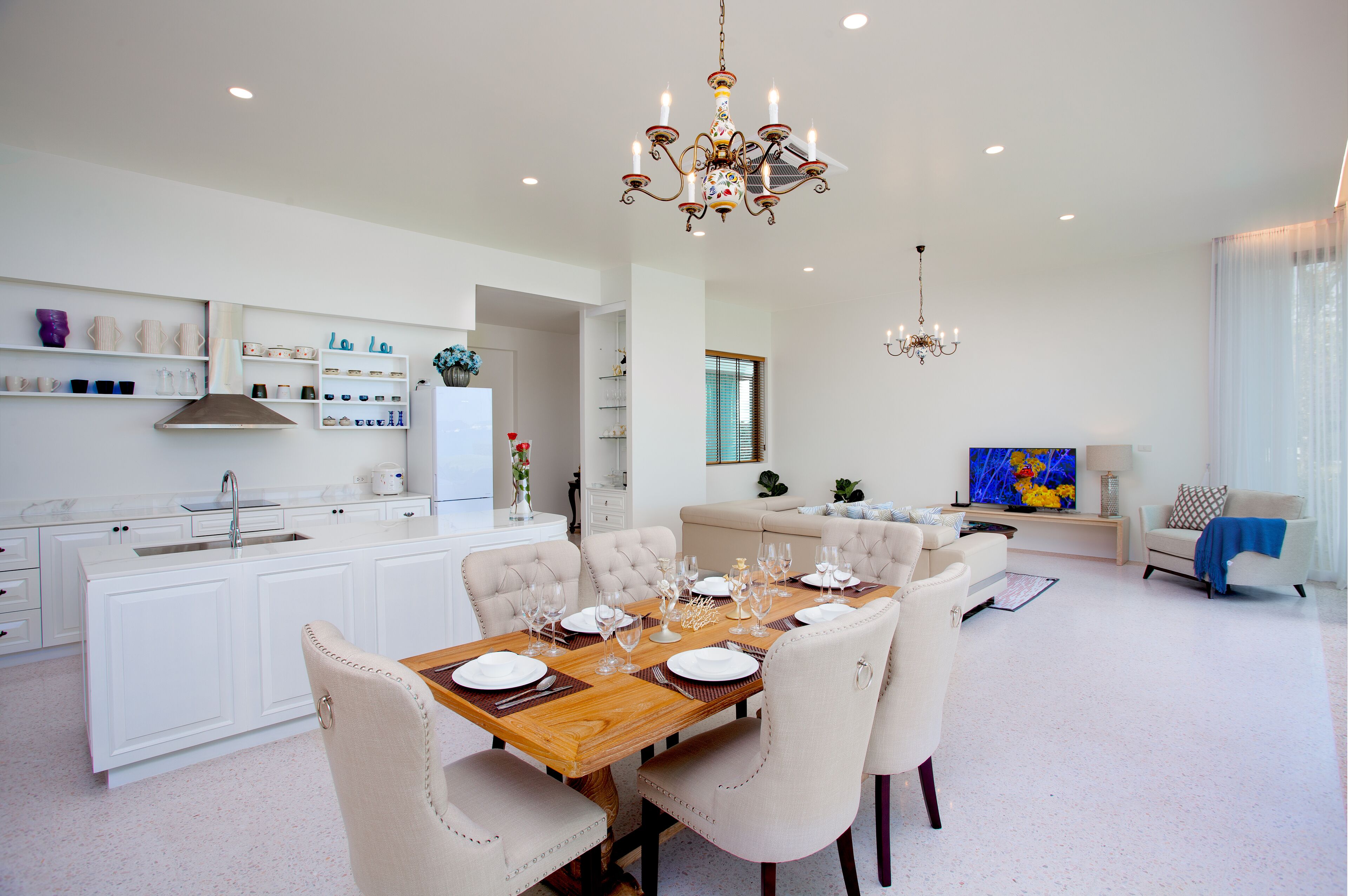 Una cocina amplia y moderna con armarios blancos, una mesa de comedor de madera preparada para seis comensales y una araña.
