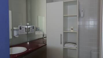 A bathroom with a white sink, a mirror, a glass-enclosed cabinet, and a toilet.