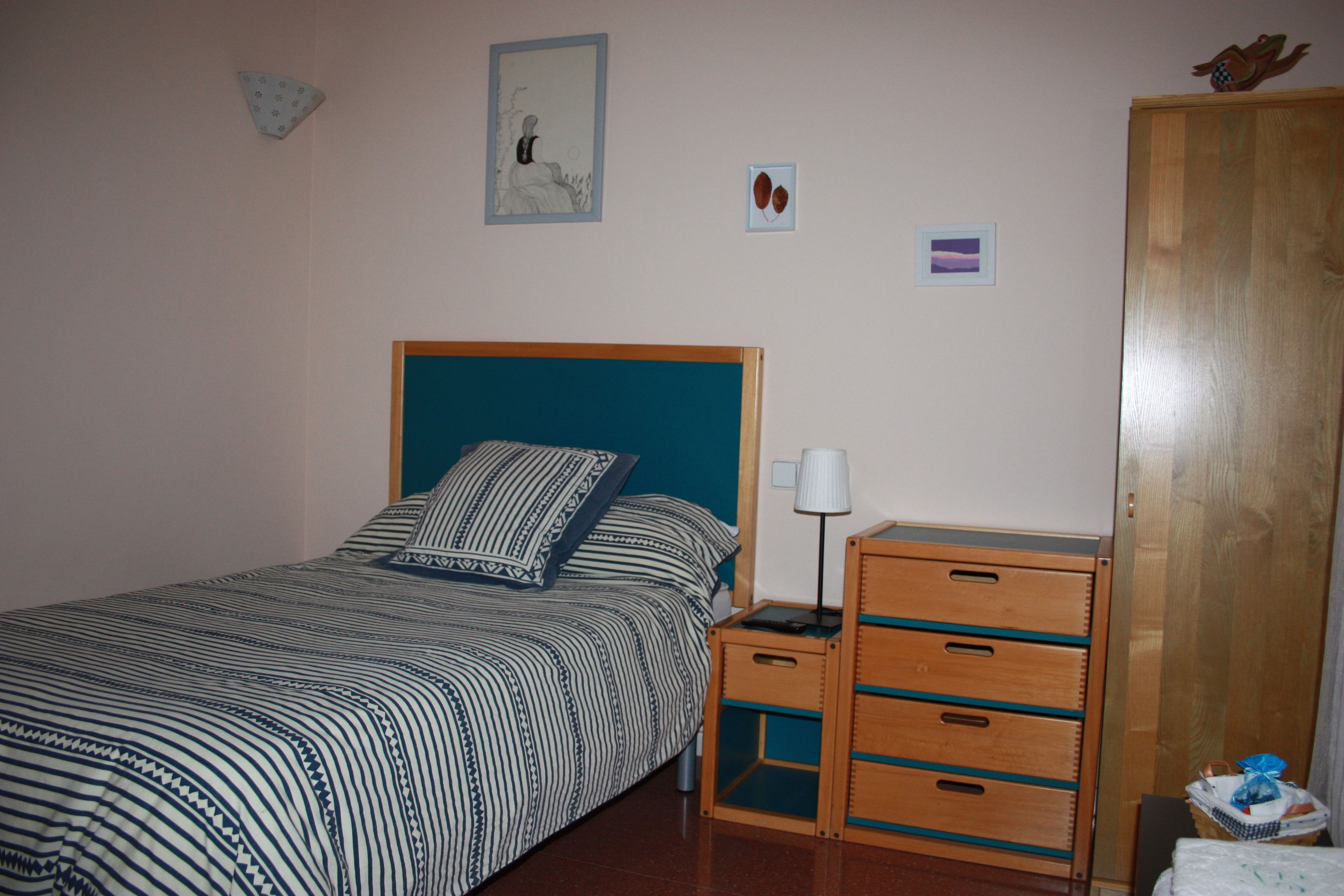 Un dormitorio con cama, mesita de noche, lámpara y un armario de madera.