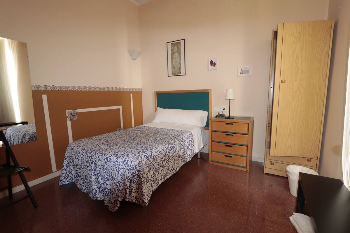 A bedroom with a bed, bedside table, wardrobe, and a chair.