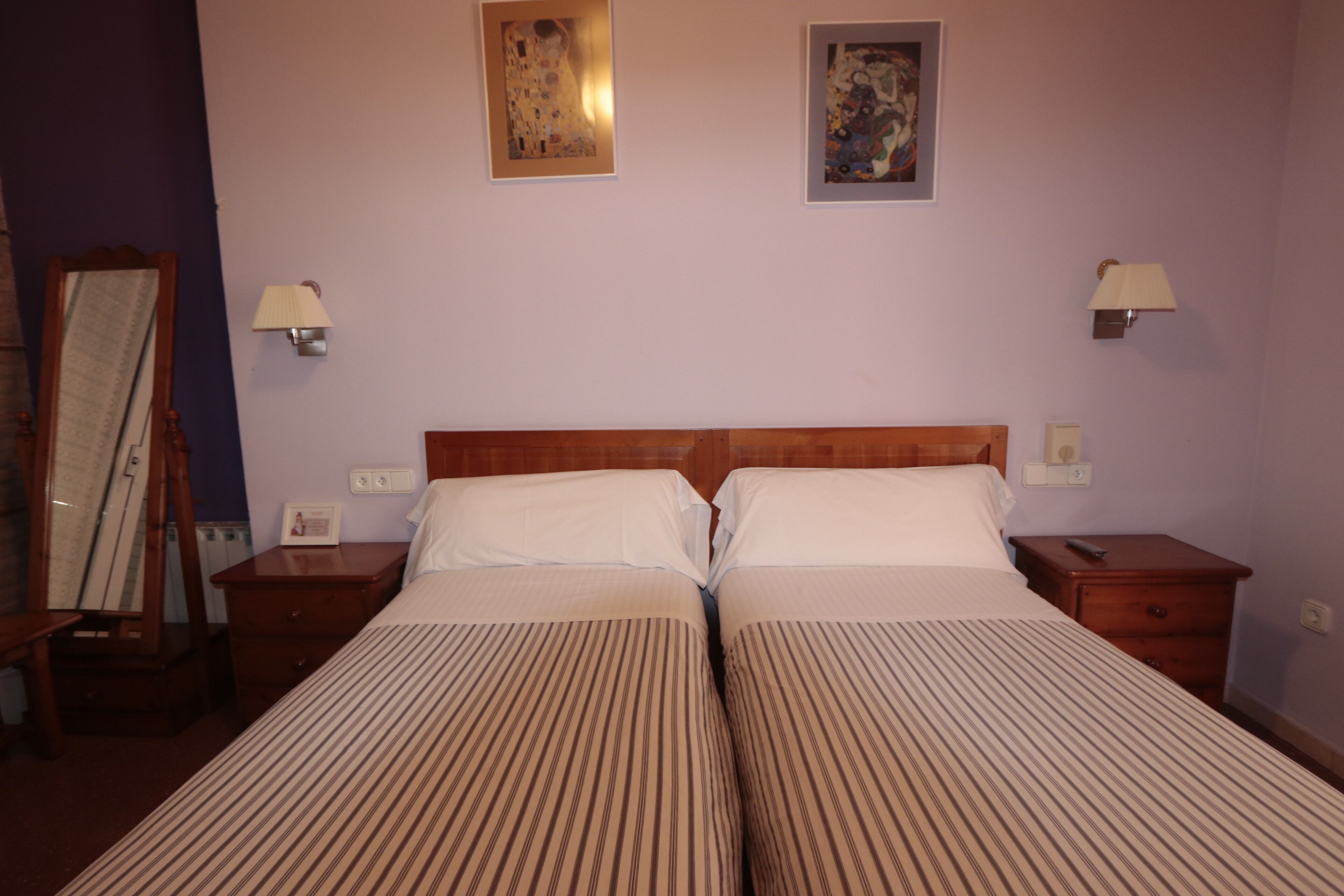 Una cama doble con ropa de cama a rayas, dos mesitas de noche, una lámpara y dos cuadros en la pared.