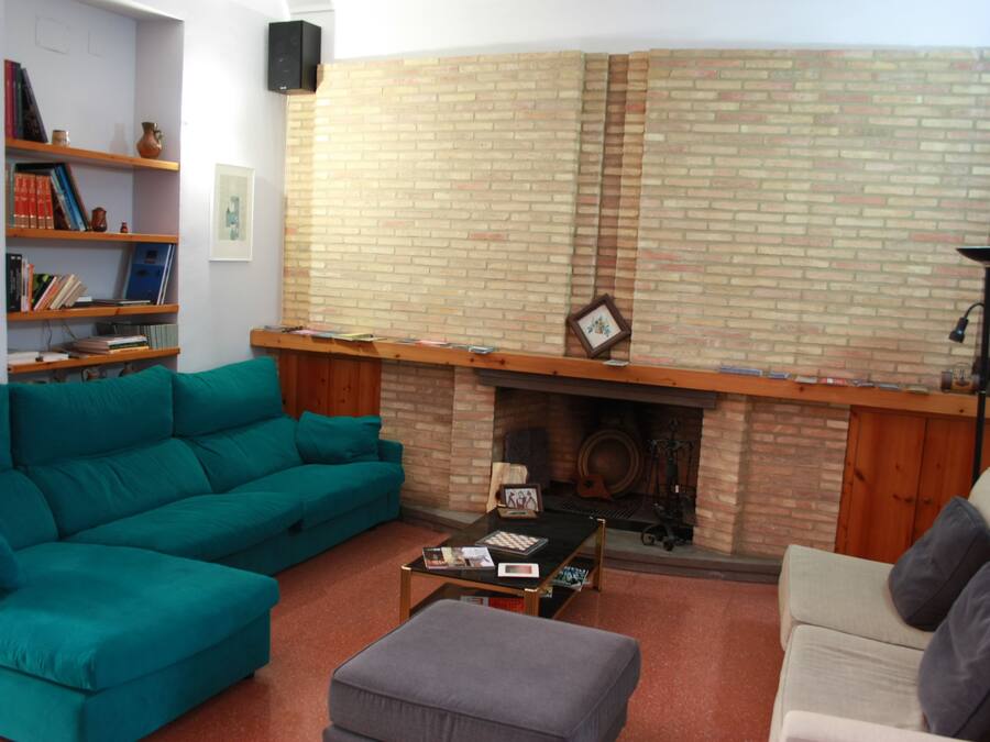 A living room with a brick fireplace, teal and beige sofas, a coffee table, and a bookshelf.