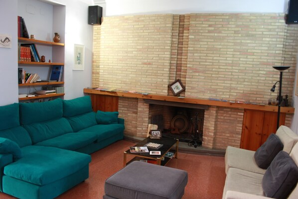 A living room with a brick fireplace, teal and beige sofas, a coffee table, and a bookshelf. - B&B Domus Atilia (Sagunto)