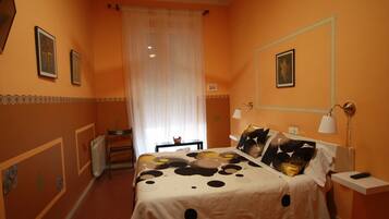 A bedroom with a bed, bedside tables, a nightstand, a window with curtains, and wall decorations.