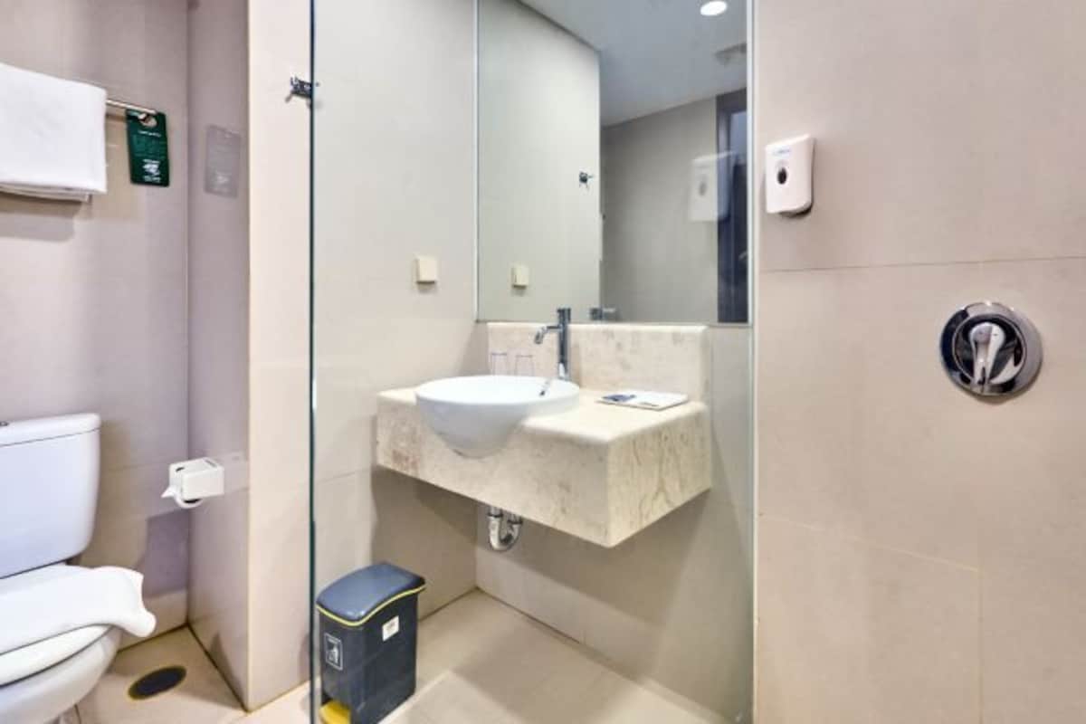 Un baño moderno con lavamanos blanco, cabina de ducha con mampara de vidrio e inodoro.