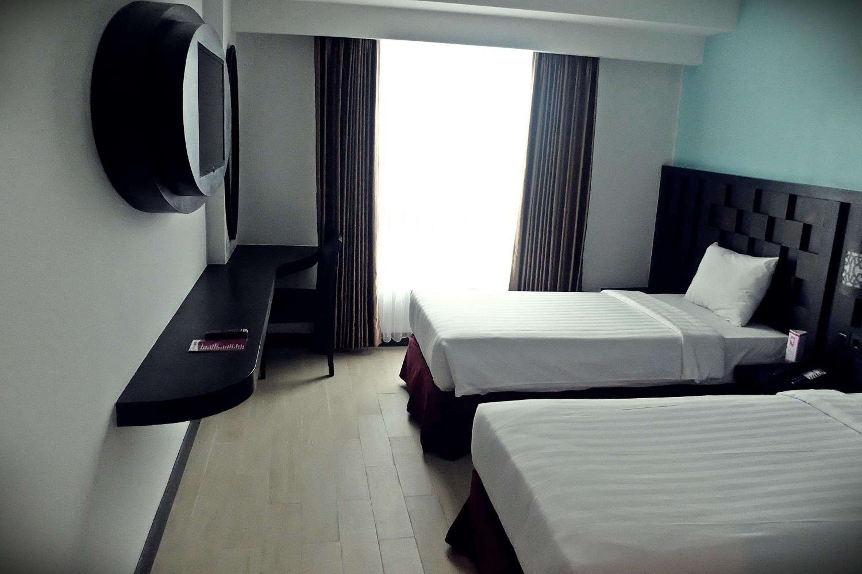 A hotel room with two beds, a TV mounted on the wall, a desk, and a window with curtains.