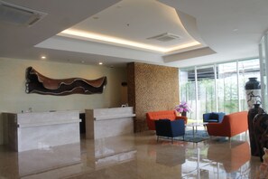 A reception area with a marble counter, two sofas, and a large window offering a view of greenery. - Grand Orchid Hotel Yogyakarta (Depok)