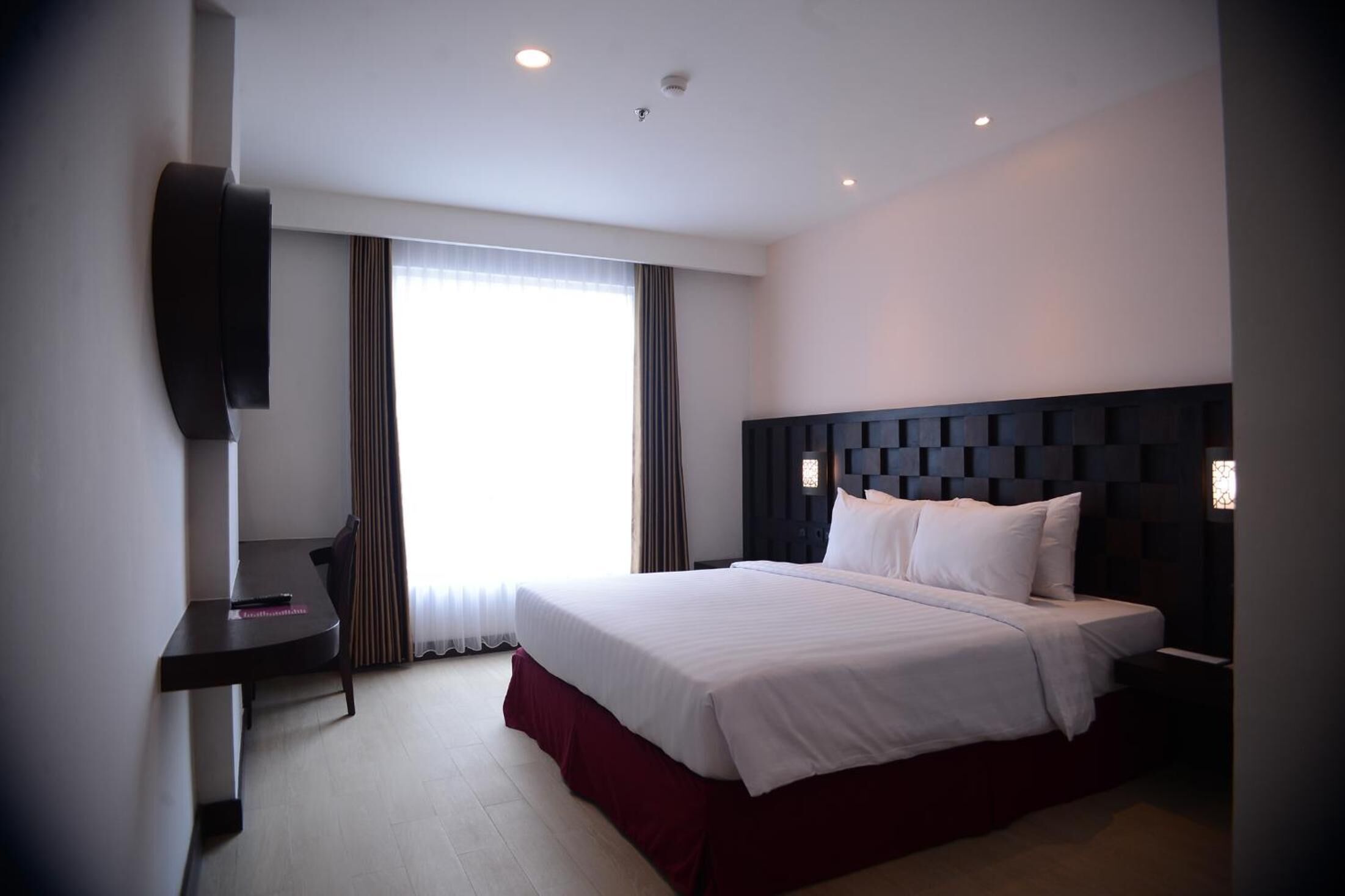 Een hotelkamer met een groot bed, een bureau en een aan de muur bevestigde televisie.