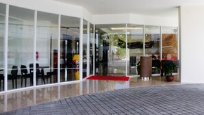 A modern building with large glass windows, a red carpet entrance, and outdoor seating. - Grand Orchid Hotel Yogyakarta (Depok)