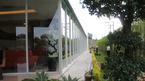 A modern building with large glass windows, a well-maintained garden with various plants, and a pathway leading to the entrance. - Grand Orchid Hotel Yogyakarta (Depok)