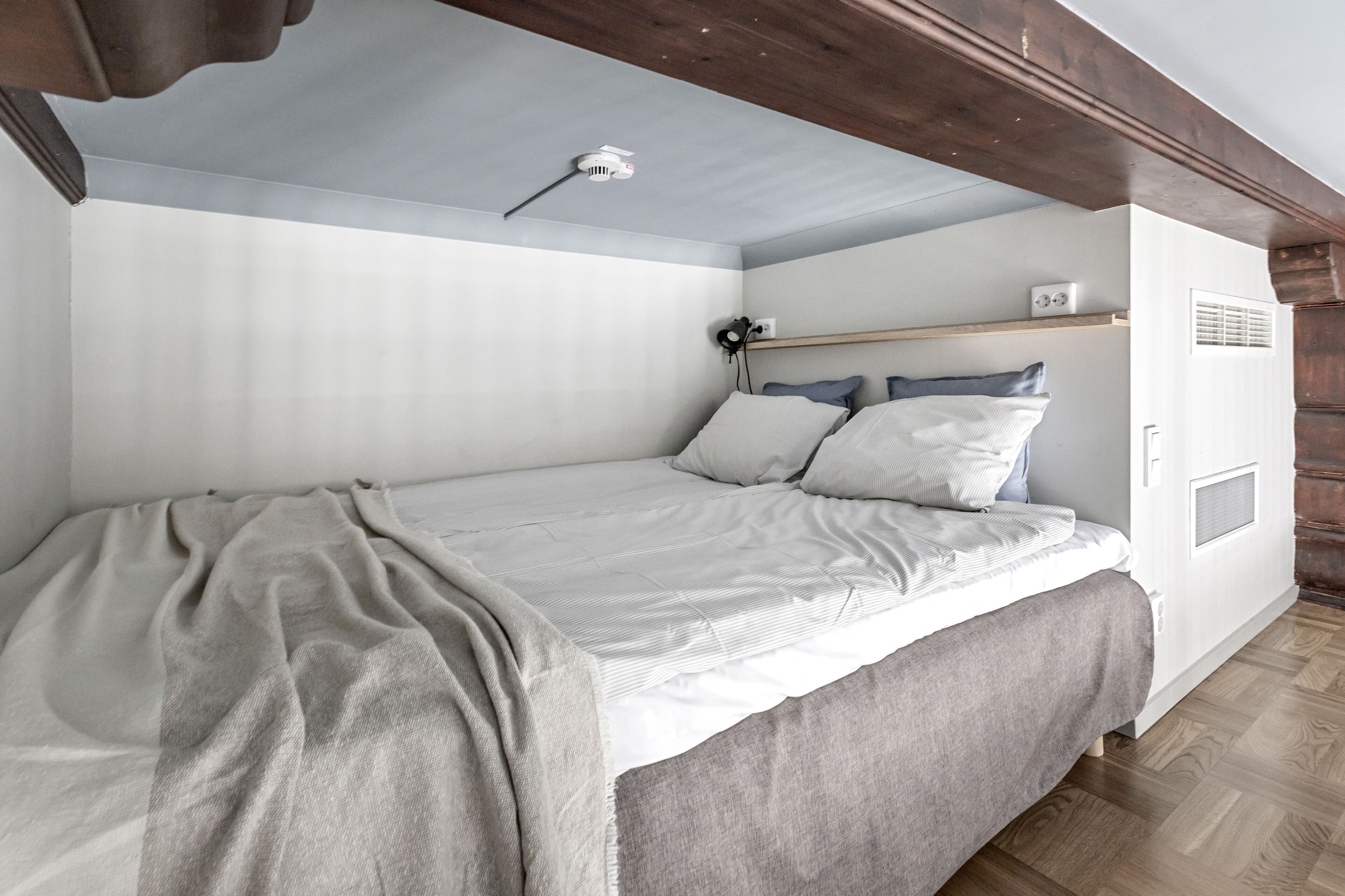A bedroom with a bed, a bedside table, a shelf, and a wall-mounted heater.