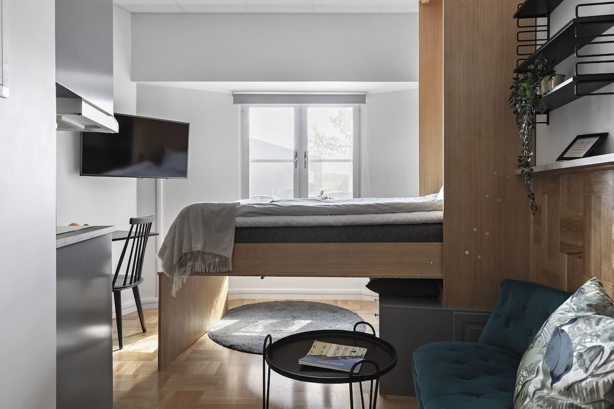 Ein gemütliches Schlafzimmer mit Etagenbett, einem kleinen Tisch mit einem Buch, einem Sessel und einem an der Wand befestigten Fernseher.
