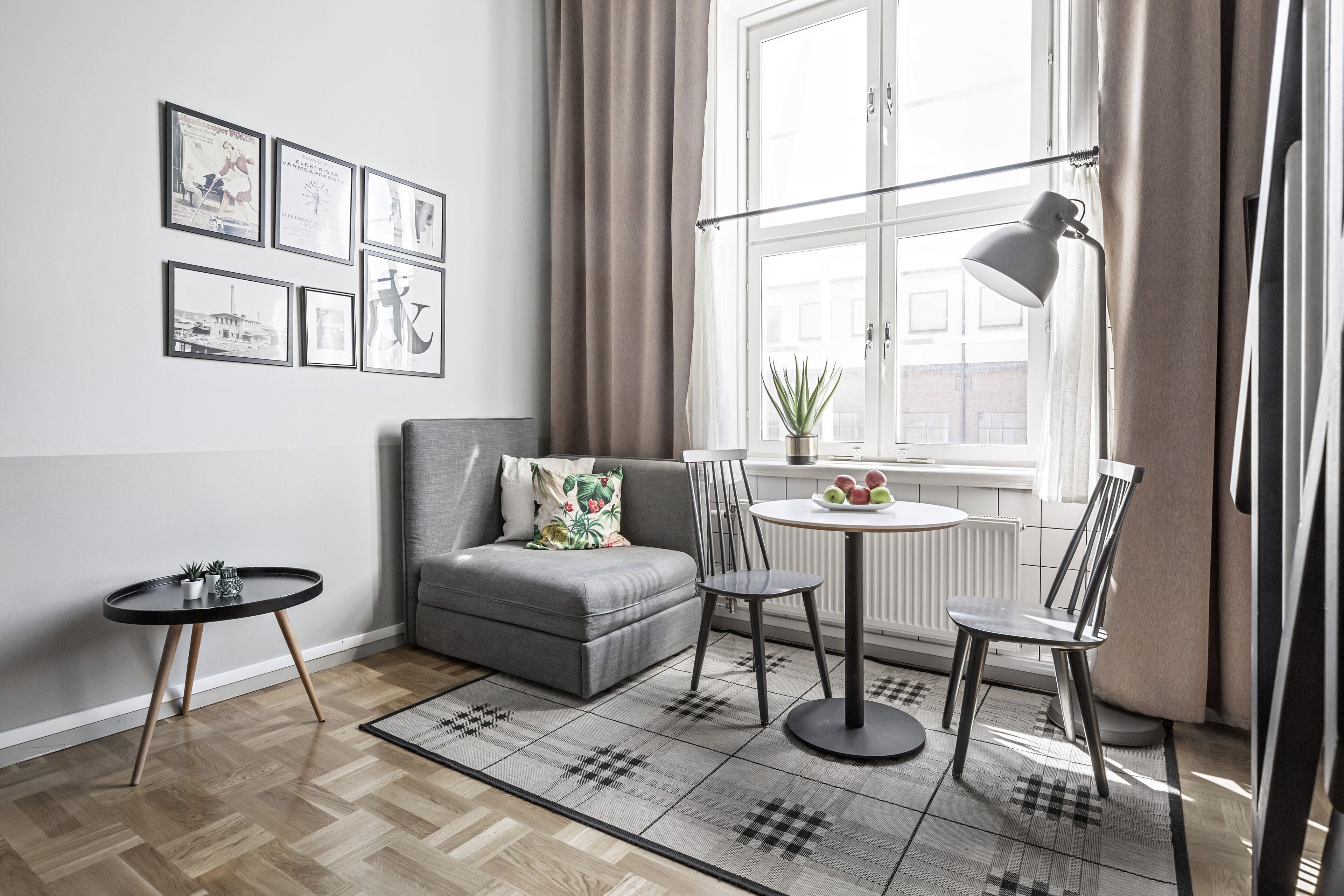 A modern living room with a grey sofa, a small round table, a floor lamp, and a window with curtains.