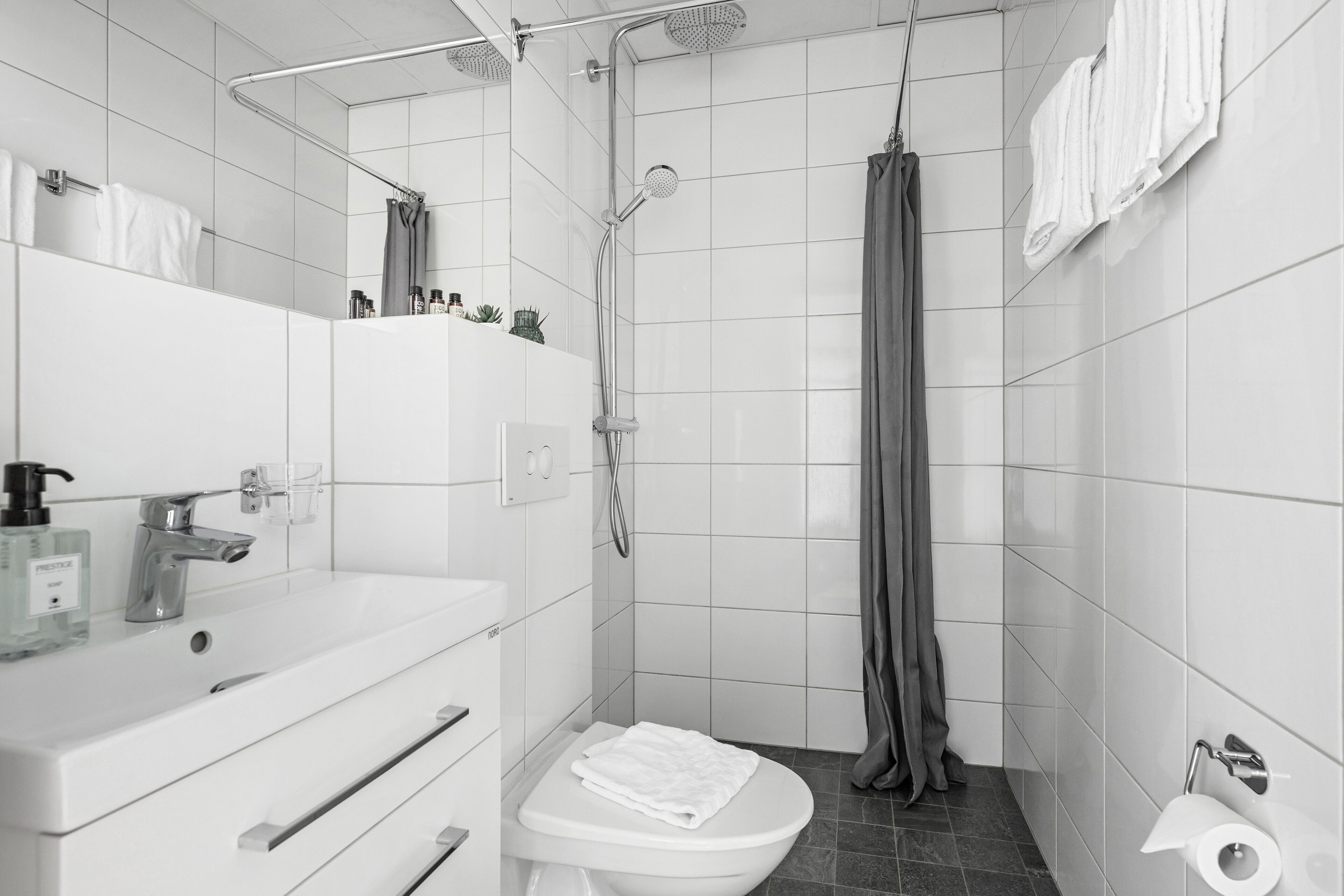 Une salle de bain moderne avec un lavabo, des toilettes et une douche, le tout de couleur blanche.