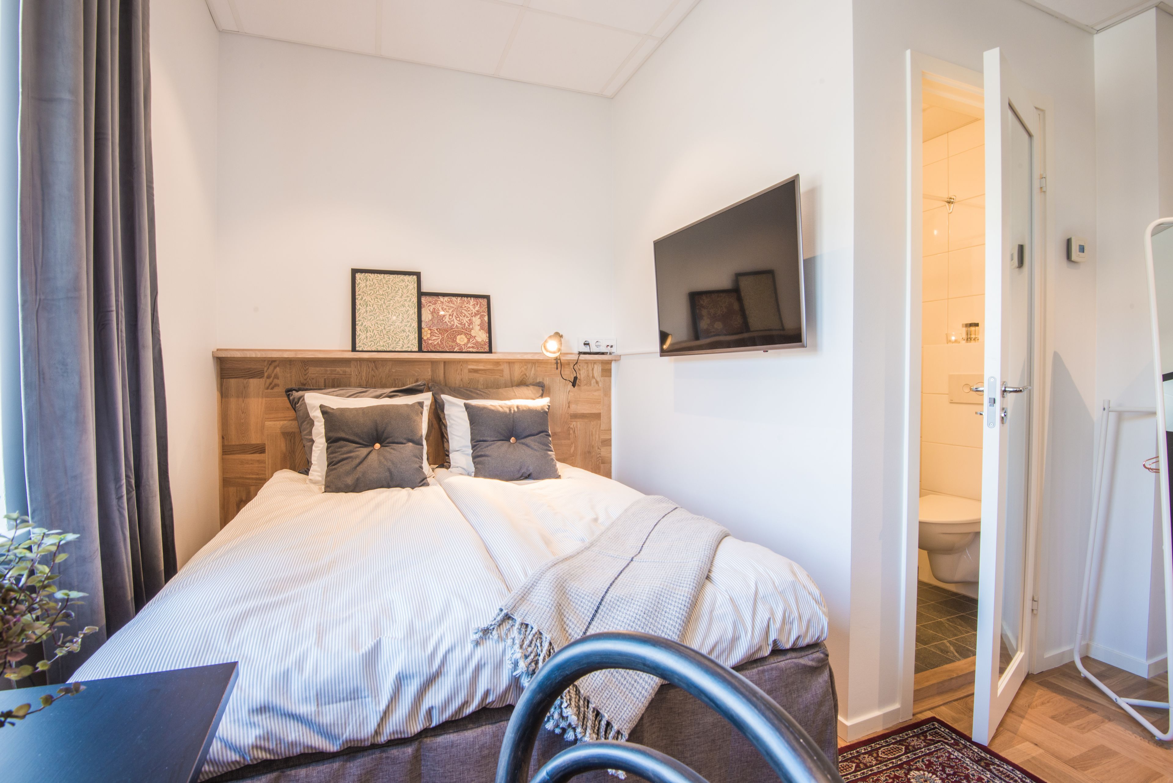 Ein modernes Schlafzimmer mit einem Holzkopfteil, einem Bett mit gestreifter Bettwäsche, einem Nachttisch und einem Spiegel an der Wand.