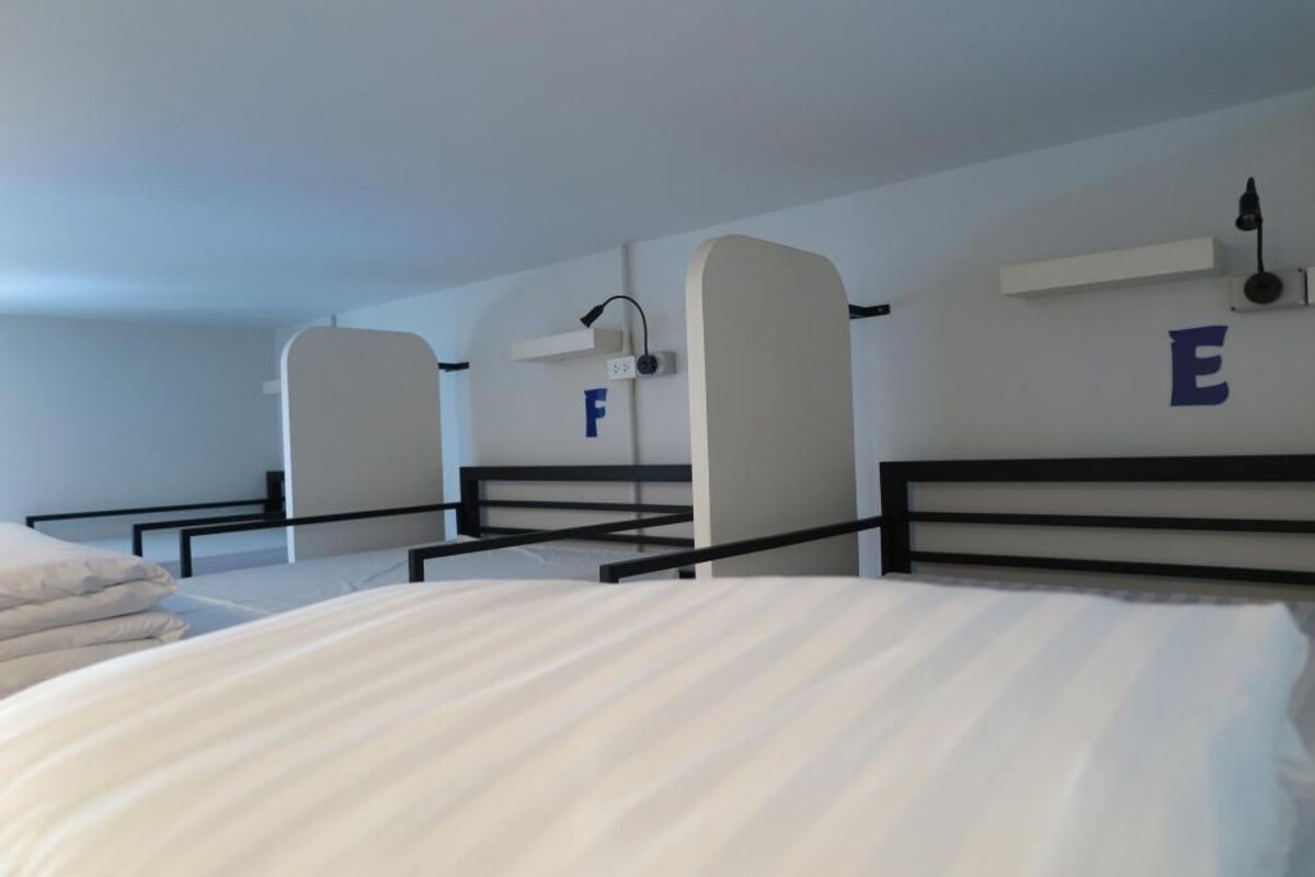 A hotel room with bunk beds, a bed with a white comforter, and a wall-mounted shelf with a lamp.