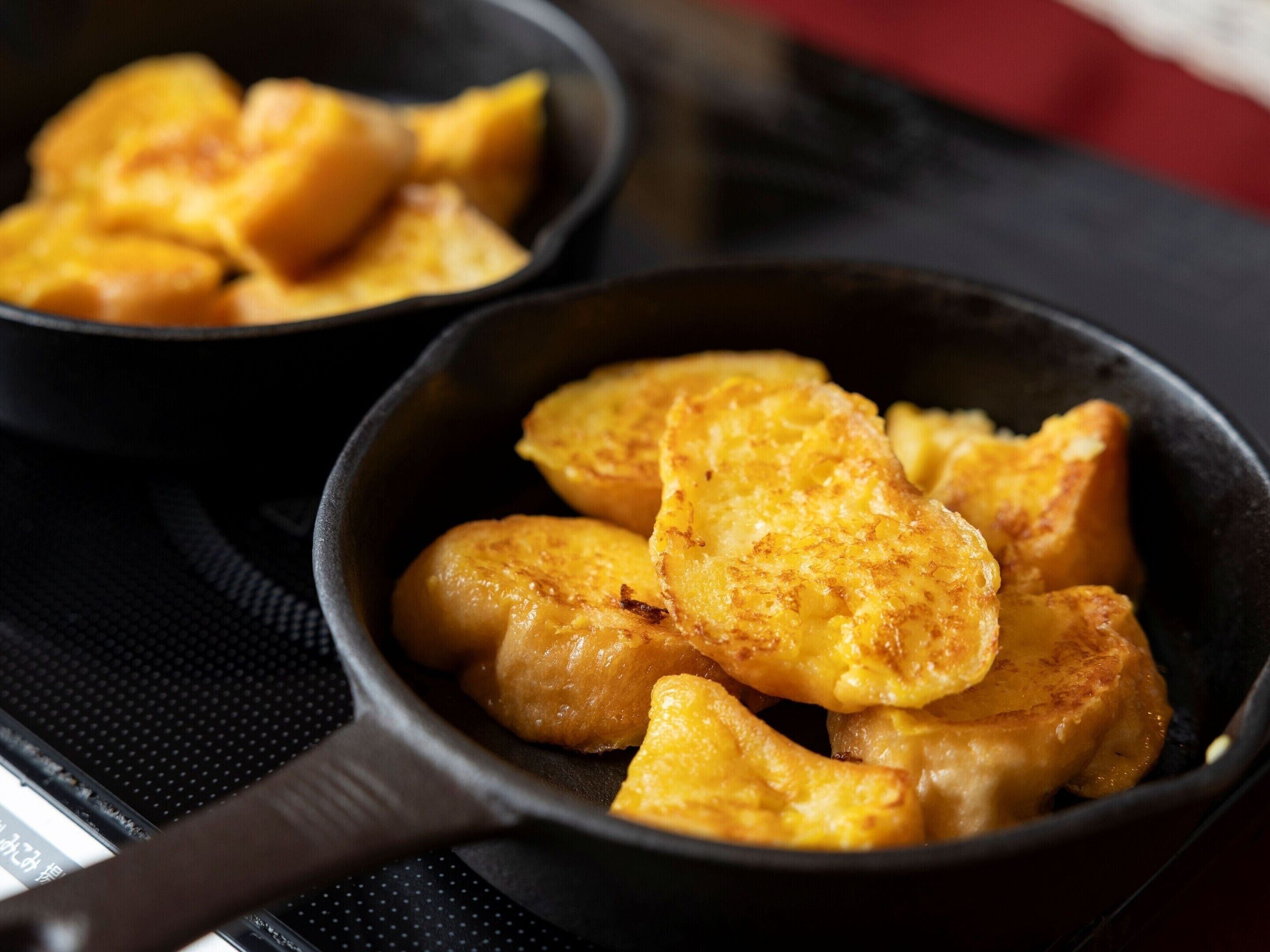 A skillet with golden-brown food items, possibly fried potatoes, on a stovetop.
