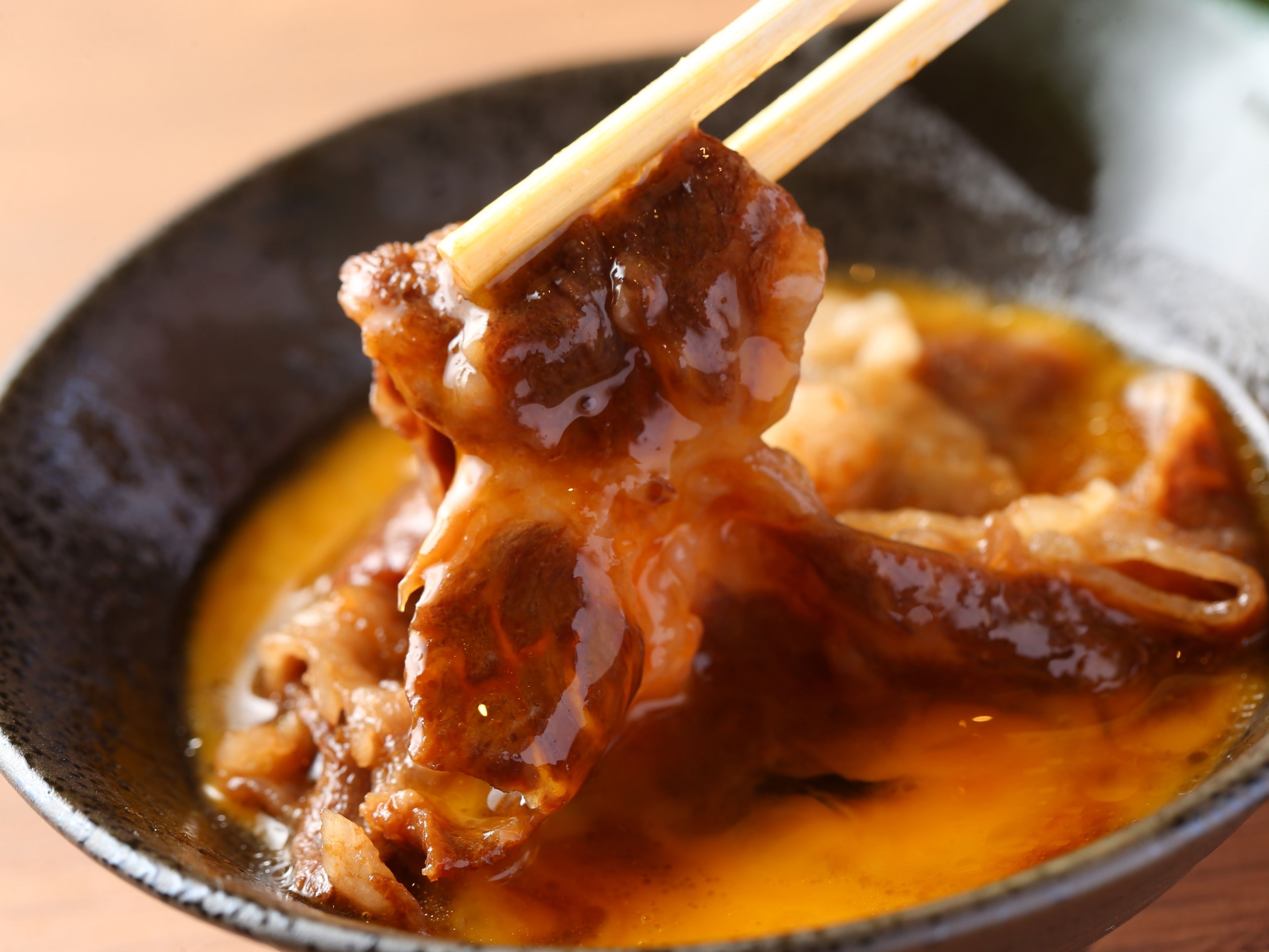 A bowl of food with a glossy sauce, held by chopsticks.